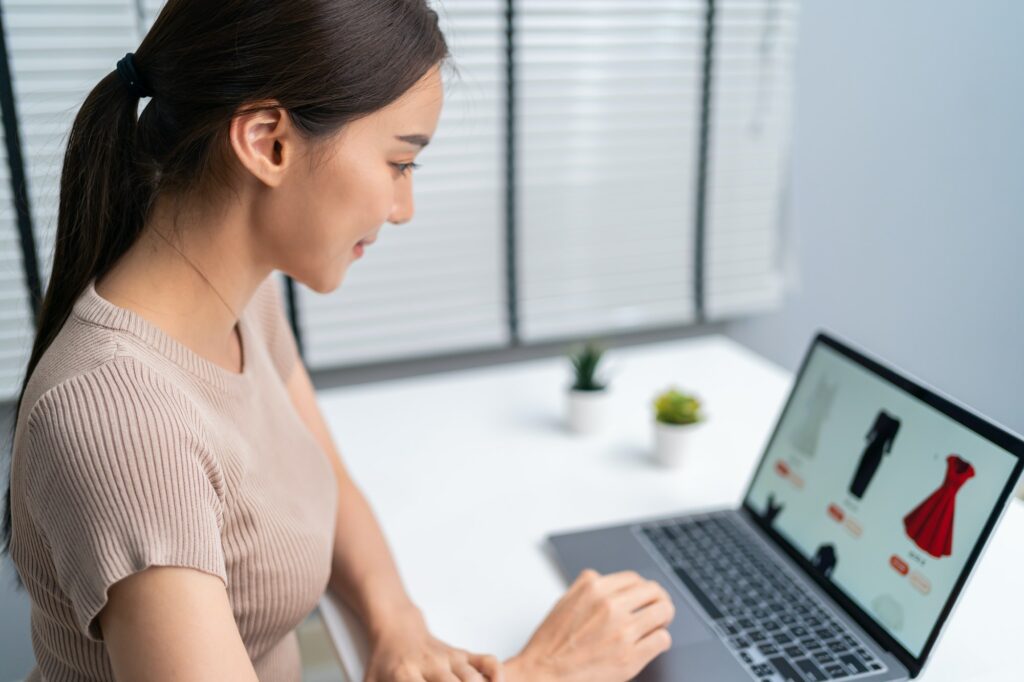 Asian young woman use laptop computer for shopping product sell online on website in smartphone.